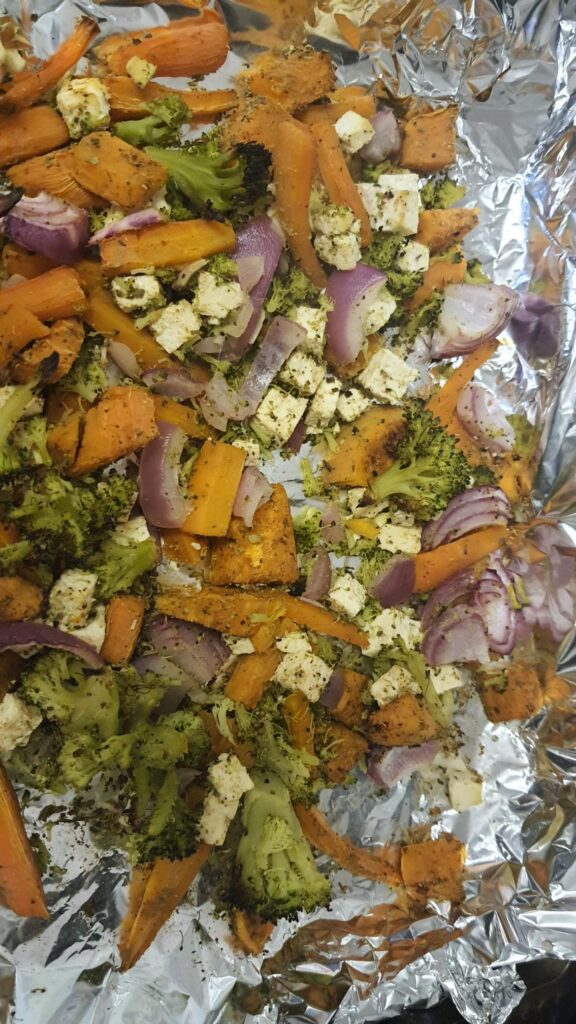 Roasted vegetables on a roasting tray including broccoli, sweet potatoe, carrots, red onion and tofu. 